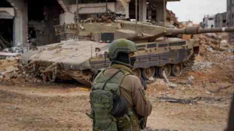 A soldier stands in front of a tank in a bomb-damaged part of Palestine